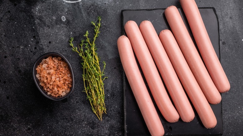 An overhead shot of raw hot dogs on a stone cutting board
