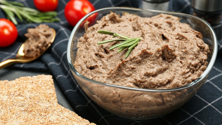 Liver pate garnished with rosemary in a glass bowl on a dark tablecloth