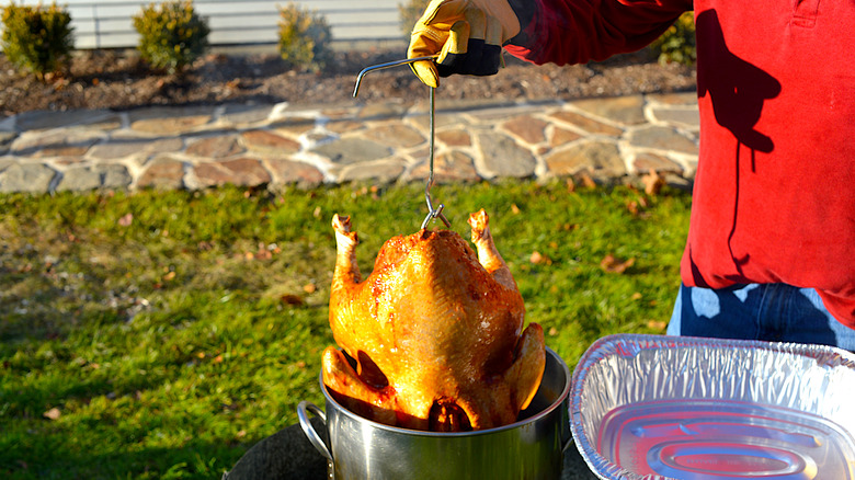 A whole turkey being lowered into a vat of oil outdoors