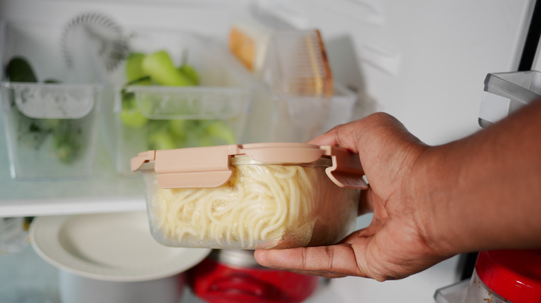 Someone pulling a container of leftover spaghetti out of a refrigerator