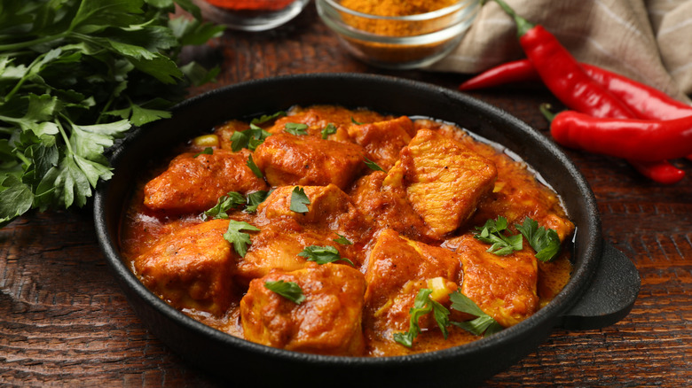 Chicken tikka masala in a cast iron bowl surrounded by fresh ingredients and spices