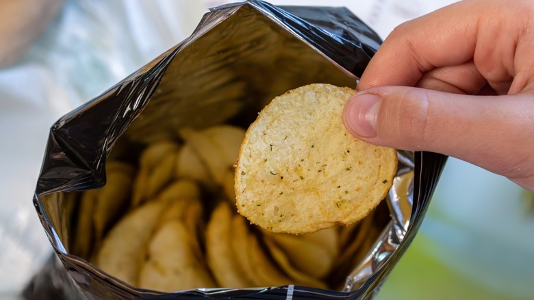 Hand reaching in aluminum foil potato chip bag and taking out one chip