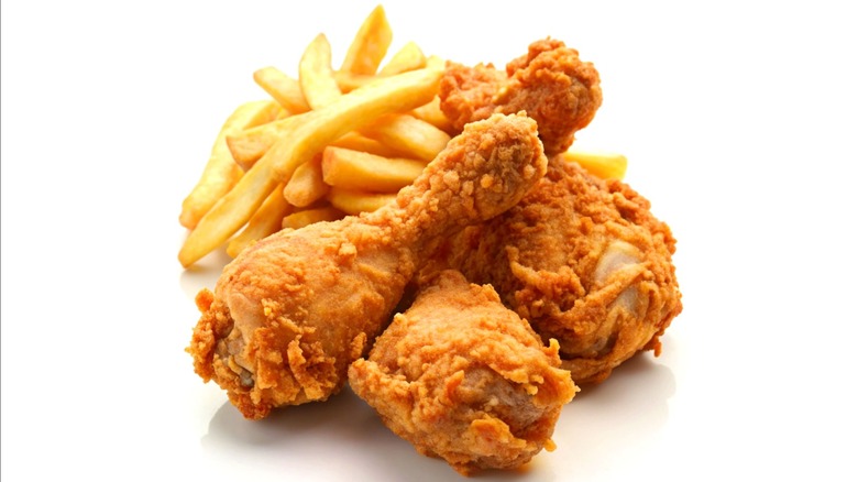 A serving of crispy fried chicken drumsticks paired with golden French fries, presented on a white background