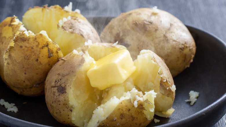 Three baked potatoes, one topped with melting butter
