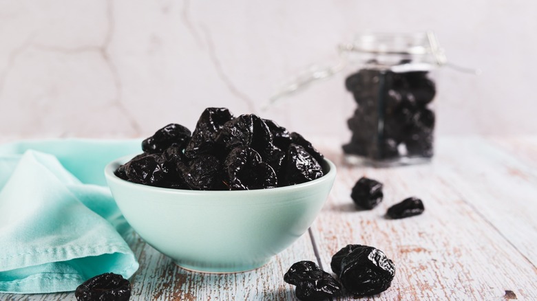 Sweet dried prunes in bowl and jar on table