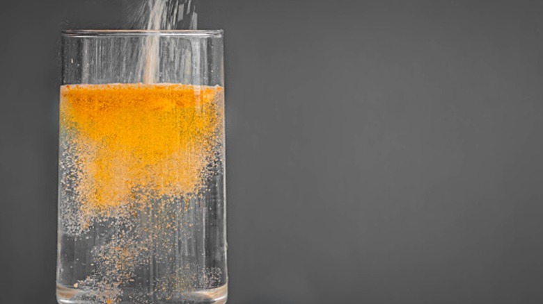 powdered drink mix being poured into a glass of water