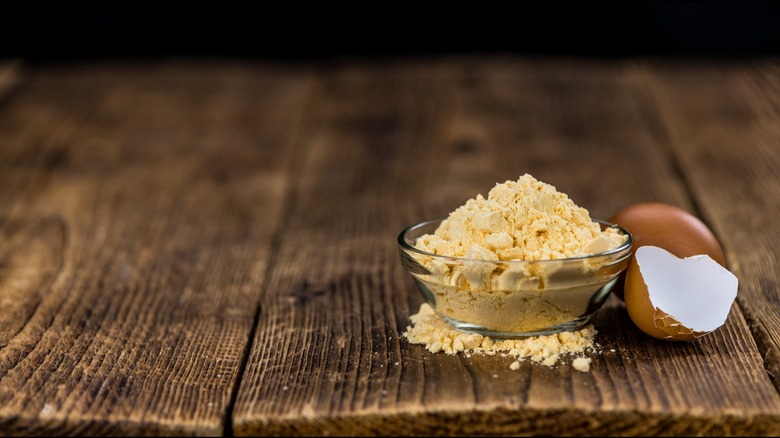 Egg powder in a glass dish beside a cracked egg shell