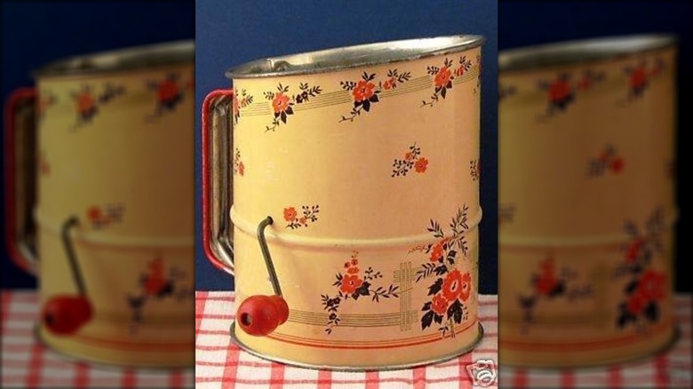 Vintage flour sifter painted yellow with floral pattern on it, and a hand crank lever