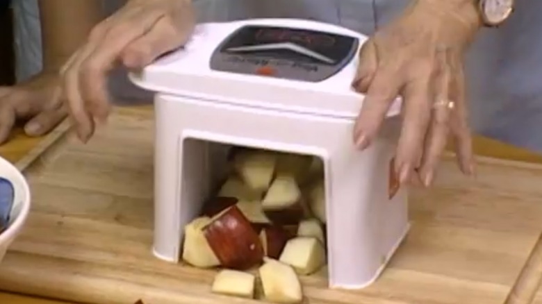 The Veg-O-Matic with a woman´s hands shown pressing down and cutting produce with it