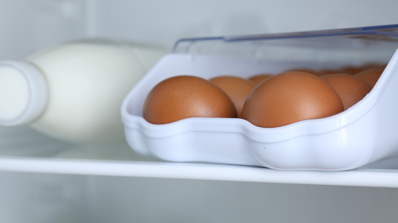 Several brown eggs rest in a plastic container in the fridge next to a bottle of milk