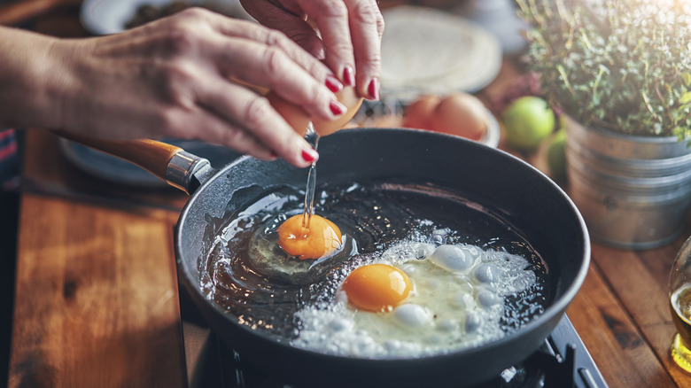 Someone cracks an egg into a sizzling frying pan