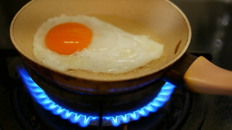 An over-easy fried egg rests in a pan over high heat