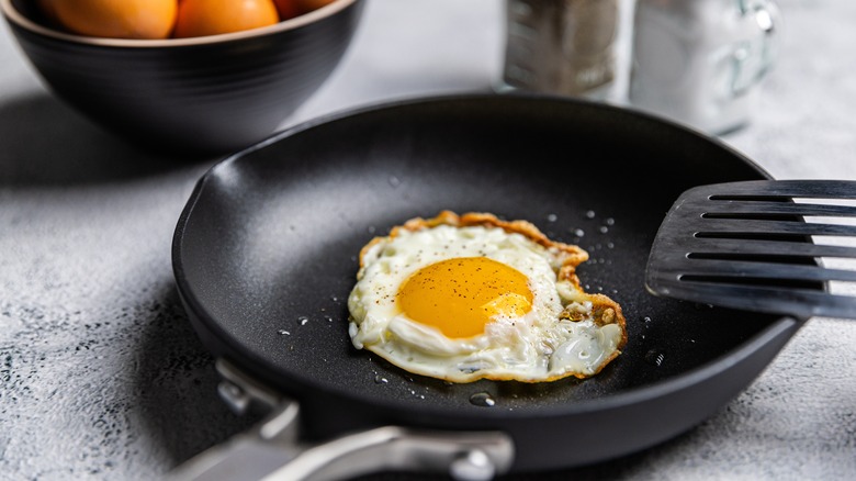 A fried egg in a frying pan with a spatula resting on the side of the pan