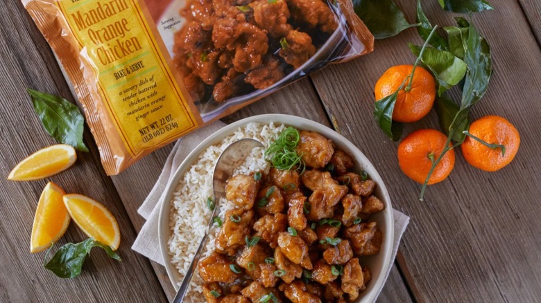 Trader Joe's Mandarin Orange Chicken served in a bowl next to the packaging and fresh oranges on a table