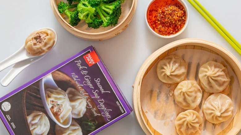 Trader Joe's Pork & Ginger Soup Dumplings styled in a steamer next to one dumpling in a spoon with a bite taken out