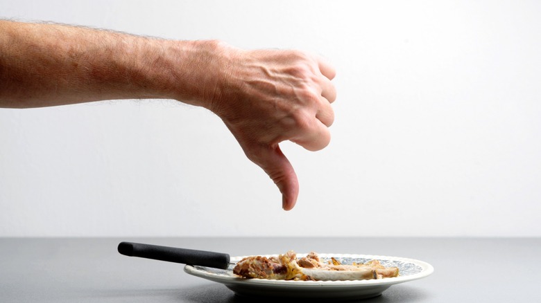 Hand shown giving a thumbs down to a plate of food