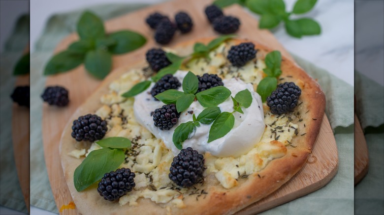 Blackberry mozzarella pizza on a table; surrounded by green leafy garnishes