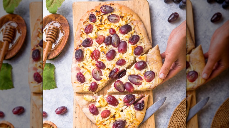 Pizza with goat cheese and red grapes on a wood board with honey on the side