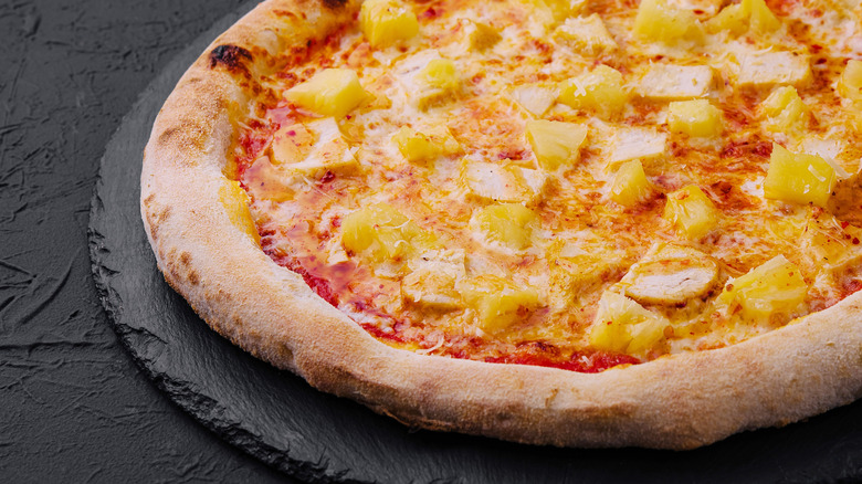 Pineapple pizza sitting on a black stone serving platter on a black textured countertop