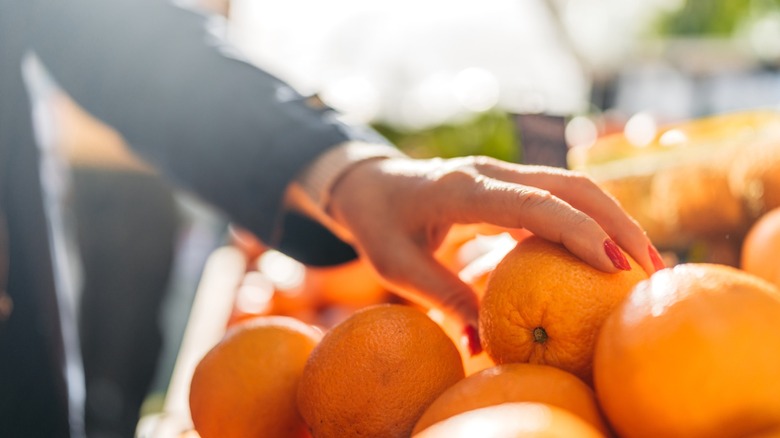 A hand feeling sweet oranges in a grocery store