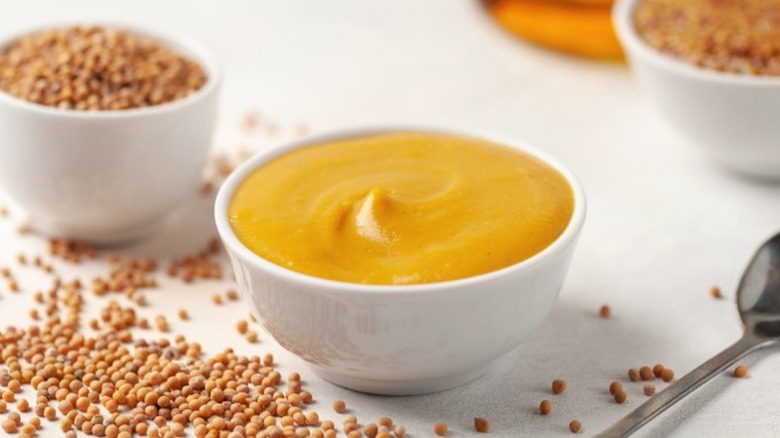 A bowl of honey mustard surrounded by mustard seeds.