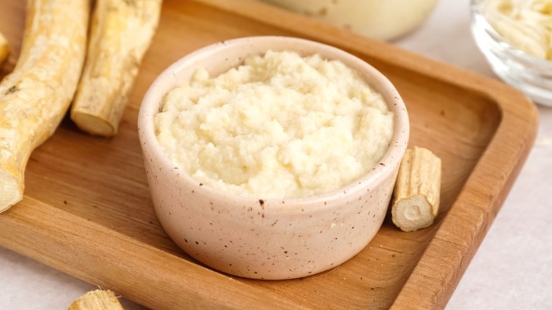Horseradish sauce in a wooden bowl next to horseradish root.