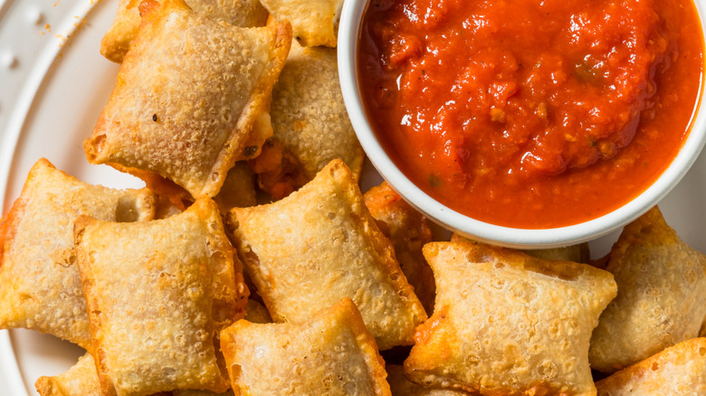 Close up of pizza rolls on plate with small cup of marinara sauce