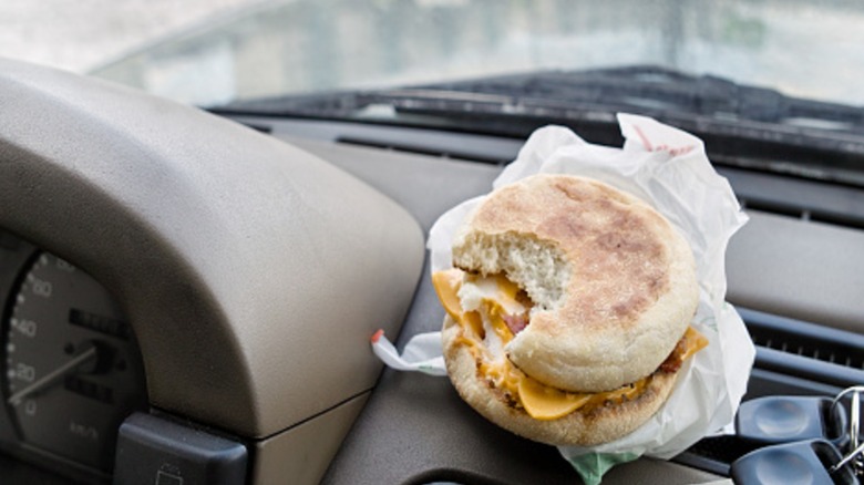 A bitten breakfast sandwich next to the ignition keys laid on a car dashboard