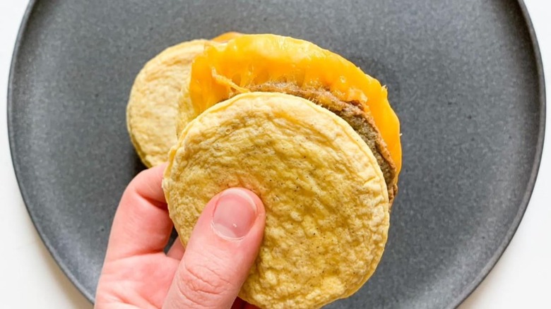 Hand holding a Trader Joe's Eggwich Breadless Breakfast Sandwich over a grey plate