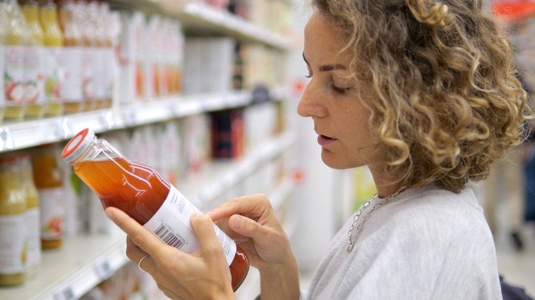 Young woman carefully reading the label of a glass bottle containing glass container of juice in a grocery store aisle
