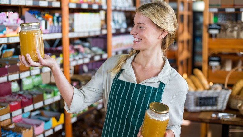 Smiling female staff holding jars of honey in super market