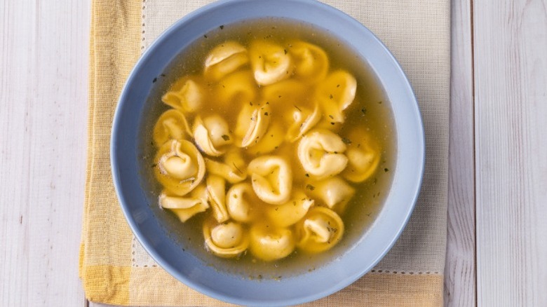 bowl of cappelletti, round hat-shaped filled Italian pasta, in a clear, yellow-tinted broth