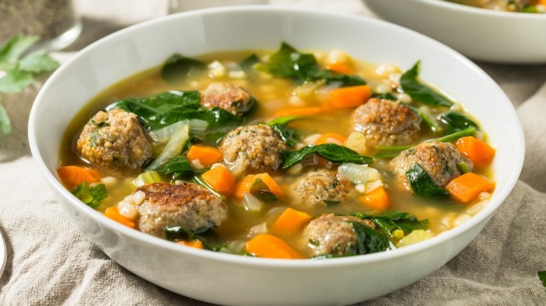 bowl of soup with small meatballs, small pasta pieces, carrots, celery, spinach, and other vegetables
