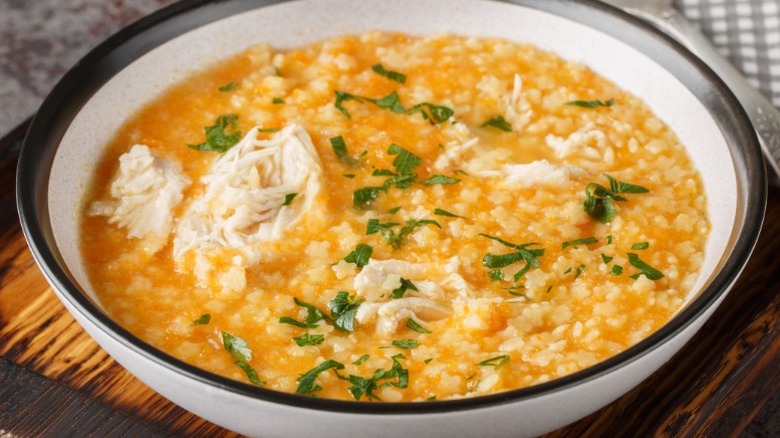 a bowl of soup with an orange colored broth, small Italian star shaped "pastina" pasta, and shredded chicken