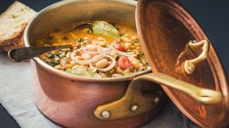 copper pot filled with a soup with cannellini beans, spinach, tomatoes and other vegetables