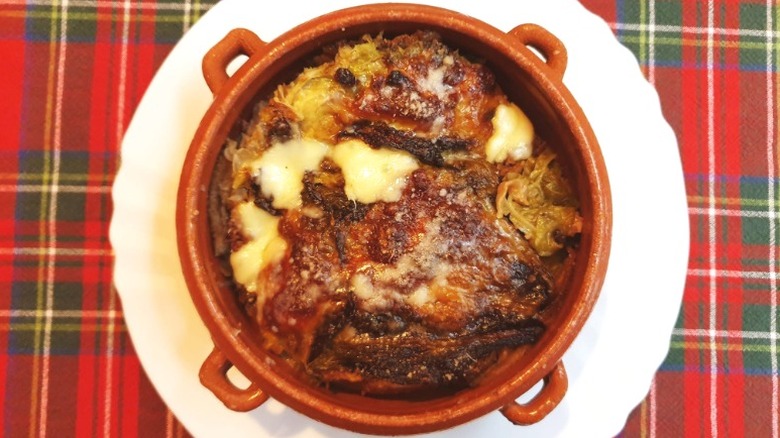 bowl of soup sits on a white plate on a red patterned tablecloth. Cabbage and bread soup baked with cheese on top