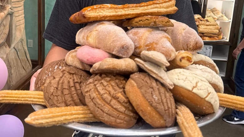 Hands holding a platter of assorted Mexican pastries and breads at El Bolillo Bakery