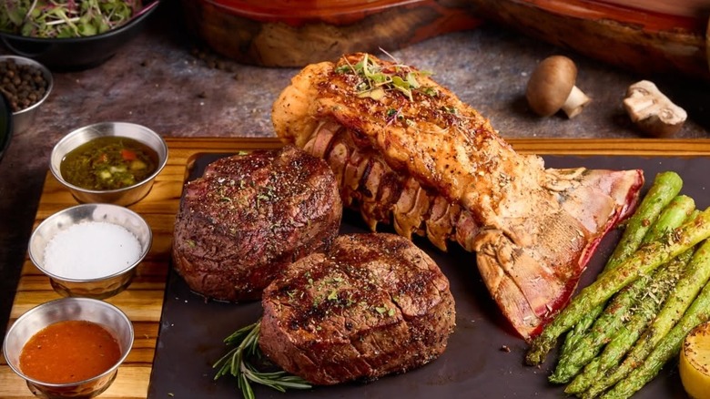 Lobster tail and two file mignons with dipping sauces and side of asparagus spears on a wooden cutting board at El Toro Loco Steakhouse