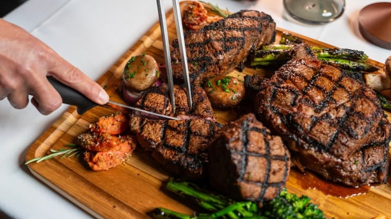 Hand shown cutting steaks on wooden cutting board at Kres Chophouse