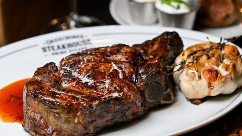 Prime dry-aged beef steak in a red wine reduction with a head of roasted garlic on a plate at Okeechobee Steakhouse