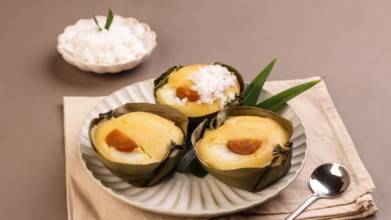Three servings of traditional Filipino bibingka in banana leaves on a scalloped plate