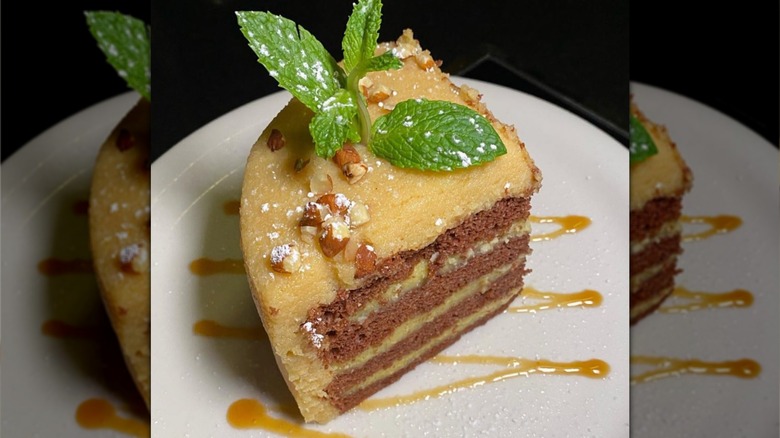 A slice of Hawaiian Chantilly Cake plated with a sprig of mint and drizzle of sauce