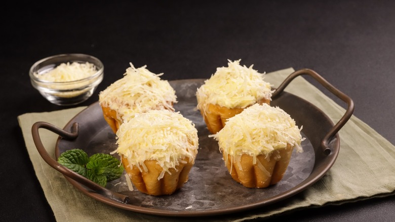 A metal tray displaying four servings of ensaymada with butter and sugar, topped with grated cheese
