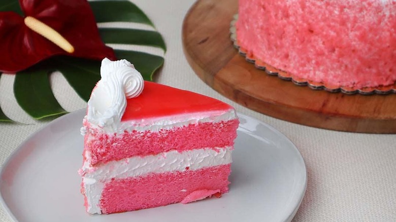 A slice of Hawaiian guava chiffon cake on a plate with the rest of the cake in the background