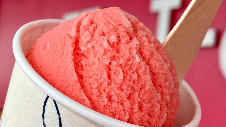 Close-up of a scoop of bright pink guri guri in a cup with a wooden spoon