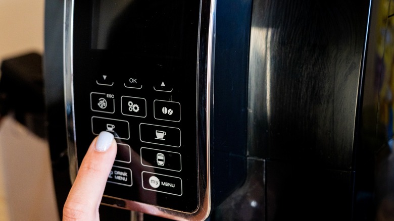 A close-up of a hand pressing the coffee selection button on a sleek coffee machine