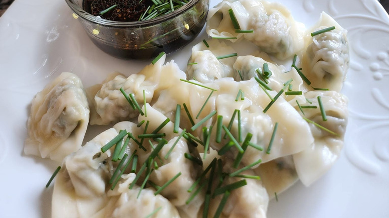 A white plate filled with Bibigo mini chicken & vegetable wontons, with a ramekin of sauce on the side
