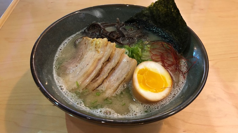 A bowl of ramen with seaweed, noodles, pork, and a soft boiled egg on a wooden table top