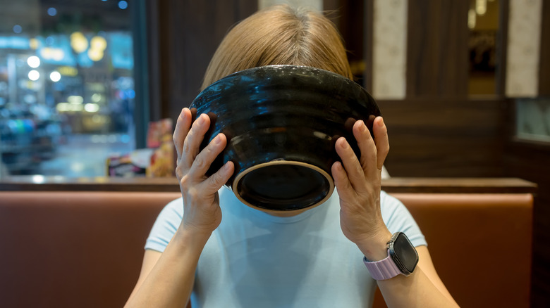 Person slurping ramen noodles from a black bowl
