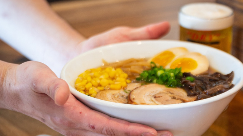 Hands holding a white bowl of ramen